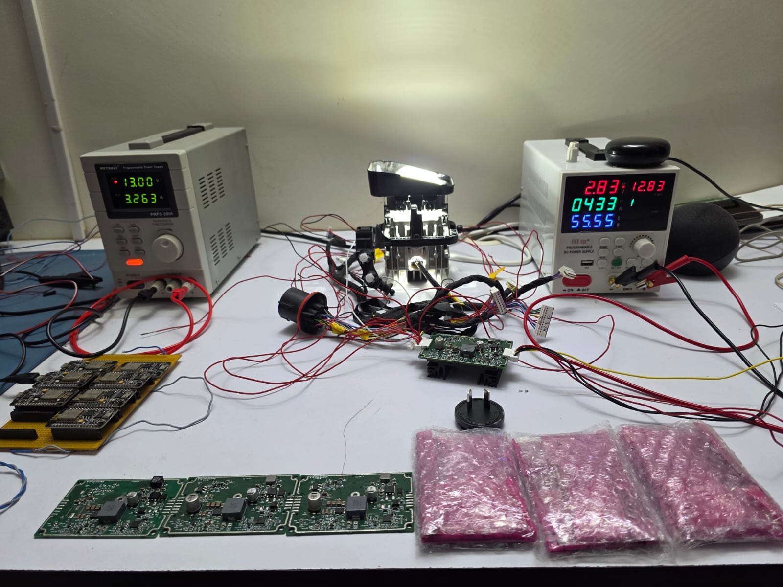 Two bench power supplies connected to circuit boards and an automotive assembly