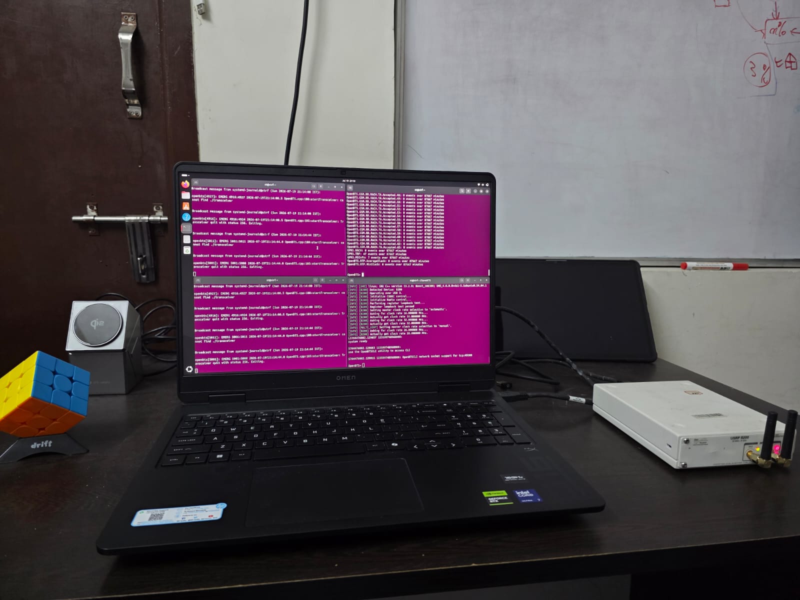 A laptop showing development logs beside a software-defined radio on a lab desk